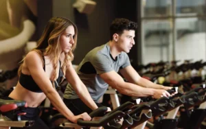 Mulher e homem pedalando em bicicletas ergométricas em aula de spinning